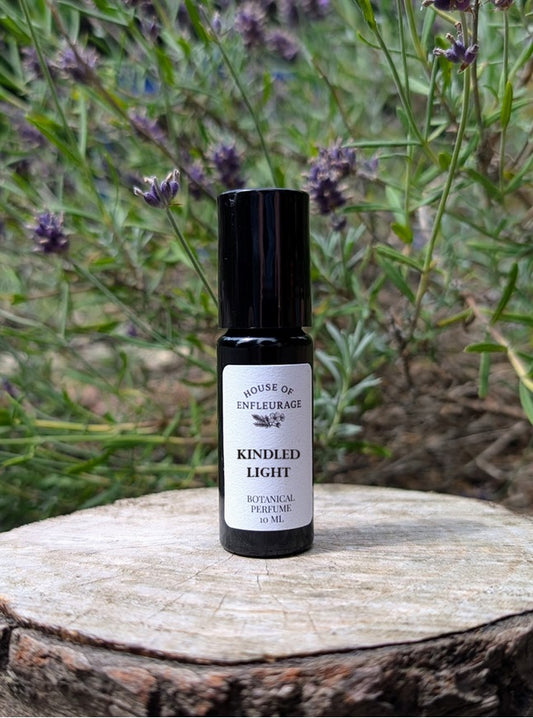 Roll-on perfume bottle labeled 'Kindled Light' on a wooden surface with lavender in the background