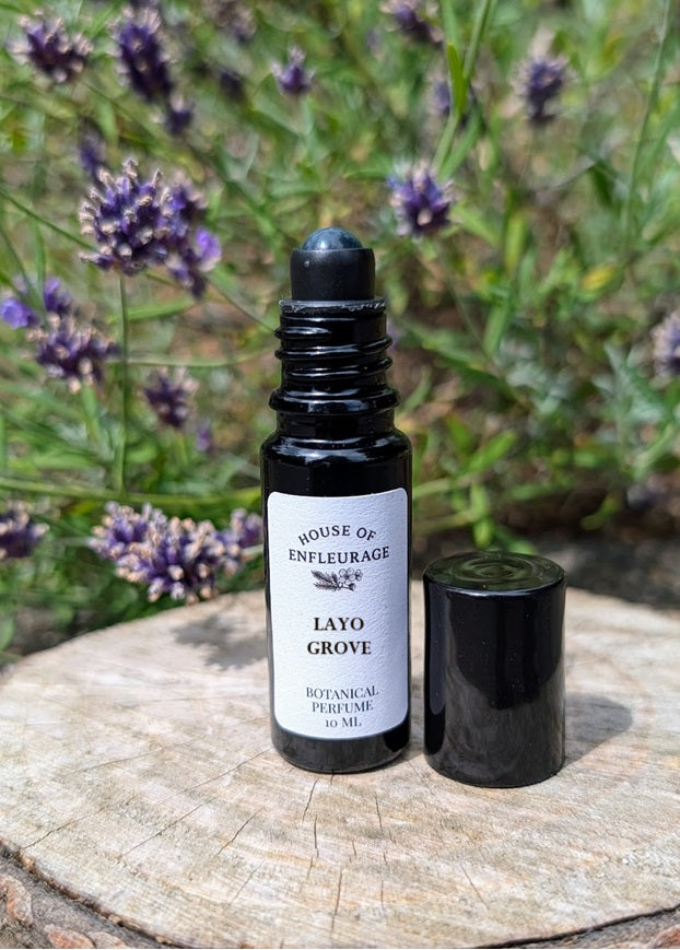 Roll-on bottle of 'Layo Grove' botanical perfume with a black cap on a wooden surface with lavender flowers in the background.